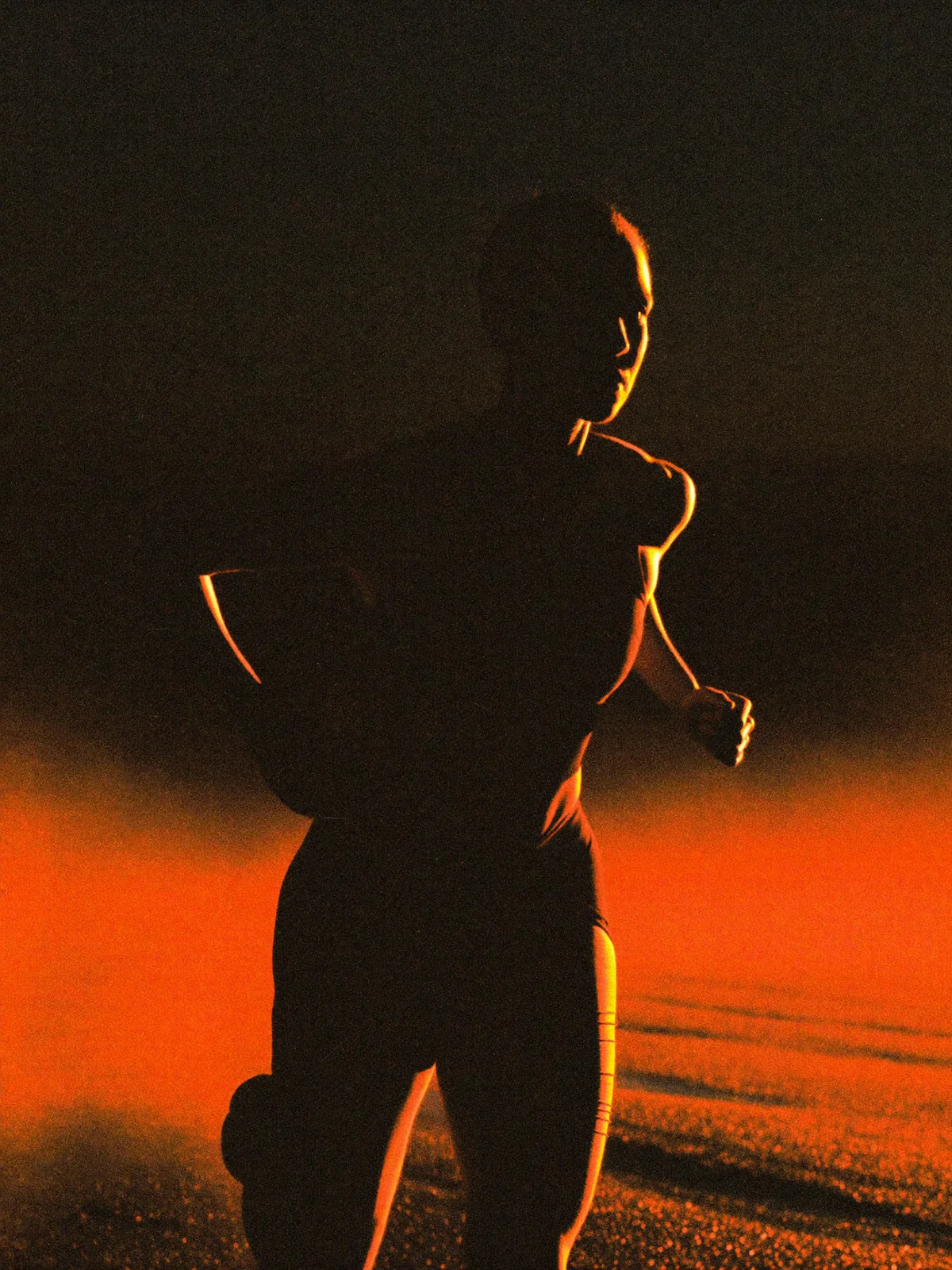 Endurance athlete running before dawn, lit by a single orange rim light
